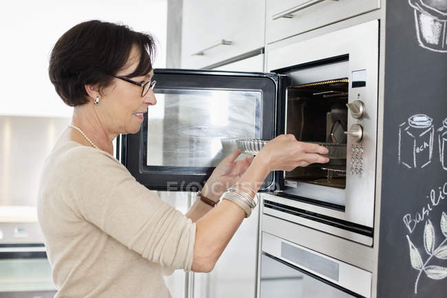 Senior woman putting tray into oven — Stock Photo