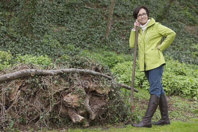 Жінка стоїть з лопатою біля купи сміття в саду — стокове фото