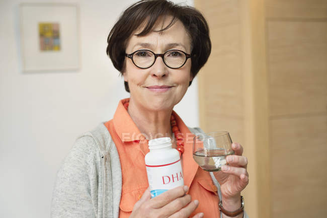 Mulher sênior segurando garrafa de suplemento alimentar na cozinha — Fotografia de Stock