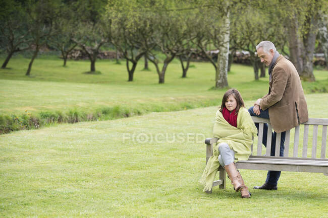 Человек, сидящий со своей дочерью на скамейке в парке — стоковое фото