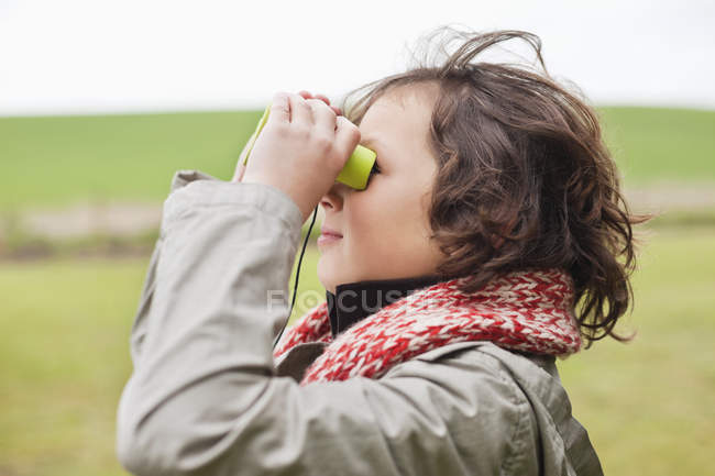 Rapaz a olhar através de binóculos no campo — Fotografia de Stock