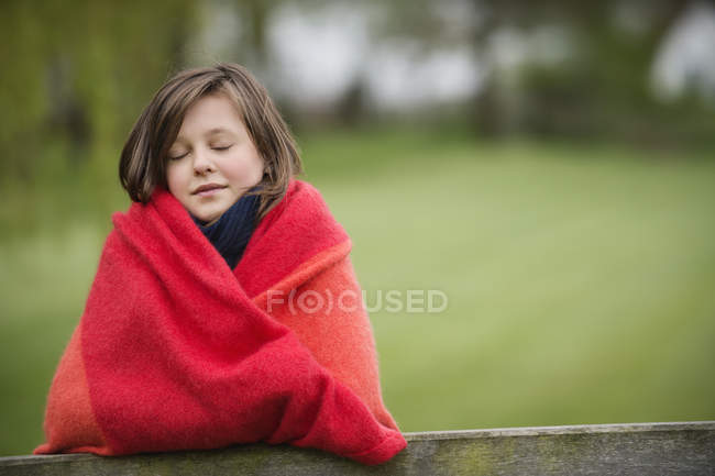 Портрет улыбающейся девушки, завернутой в одеяло, стоящей в поле на размытом фоне — стоковое фото