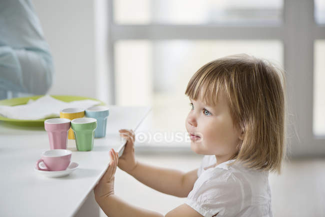 Menina bonito jogando com chá de brinquedo definido a partir de mesa de jantar — Fotografia de Stock