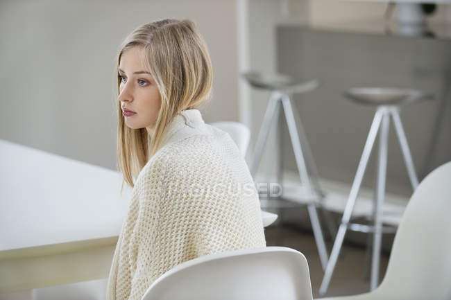 Ernsthafte junge blonde Frau sitzt im Zimmer und schaut weg — Stockfoto