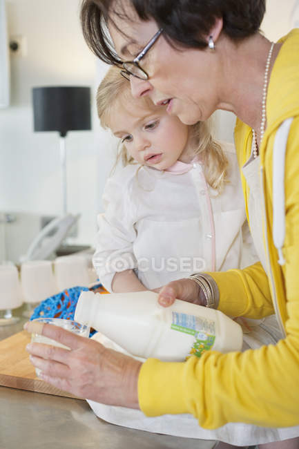Mulher sênior derramando leite em vidro para neta — Fotografia de Stock