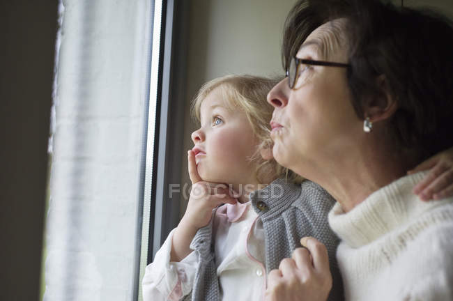 Жінка з маленькою онучкою дивиться через вікно — стокове фото