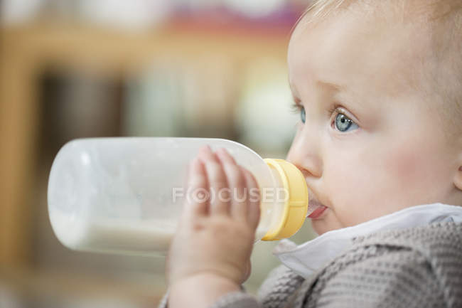 Gros plan de bébé fille aux yeux bleus nourrissant le lait — Photo de stock