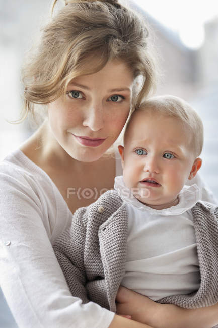 Portrait of young woman holding sad baby daughter — Stock Photo