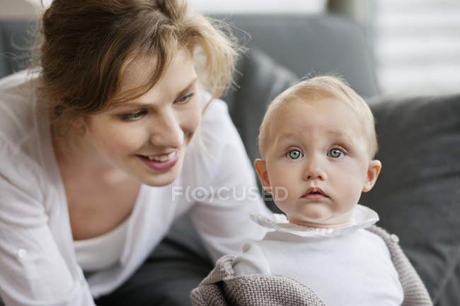Крупный план молодой женщины, помогающей маленькой дочери стоять рядом с диваном — стоковое фото