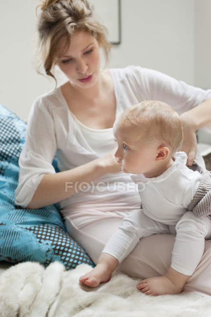 Женщина надевает одежду дочери, сидя на кровати — стоковое фото