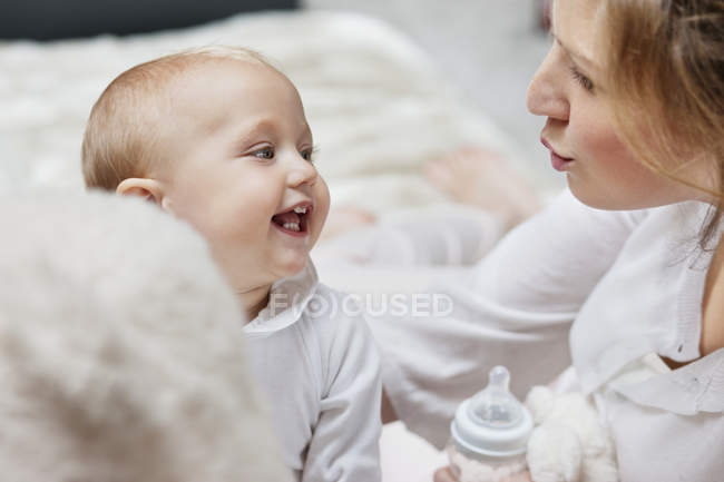 Женщина с бутылочкой, играющая с улыбающейся дочерью — стоковое фото