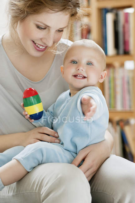 Baby girl sitting on lap of mother and playing with toy — Stock Photo
