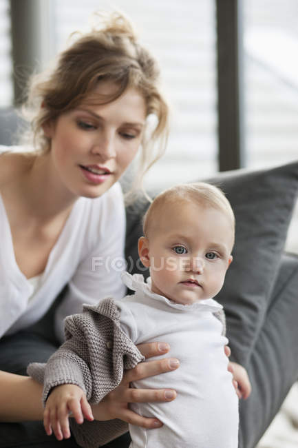 Крупный план молодой женщины, помогающей маленькой дочери стоять рядом с диваном — стоковое фото