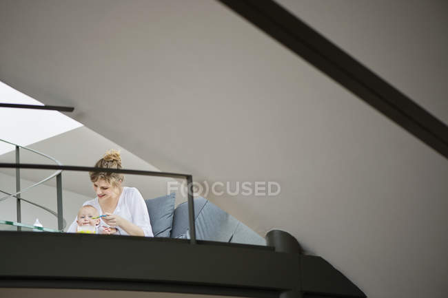 Woman feeding baby daughter next to railing at home — Stock Photo
