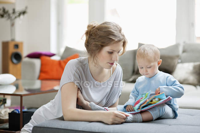 Женщина показывает книгу с картинками дочери на диване дома — стоковое фото