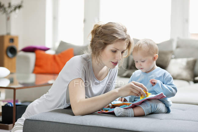 Femme montrant le livre d'image à la fille sur le canapé à la maison — Photo de stock