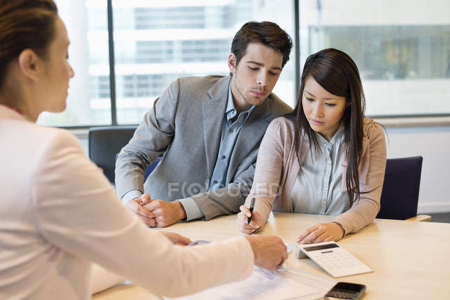Casal assinando documentos com executivo de negócios — Fotografia de Stock