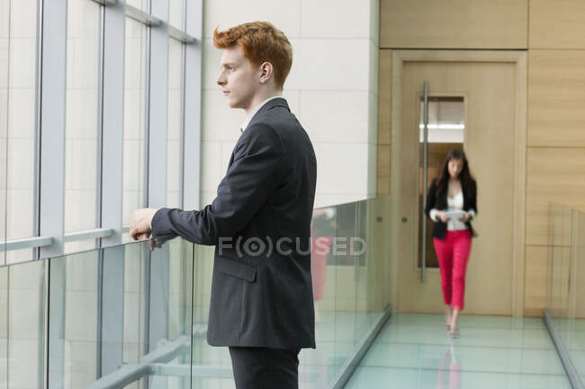 Бизнесмен смотрит через стеклянное окно в коридор — стоковое фото