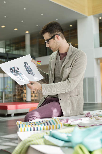 Male fashion designer holding sketches in office — Stock Photo