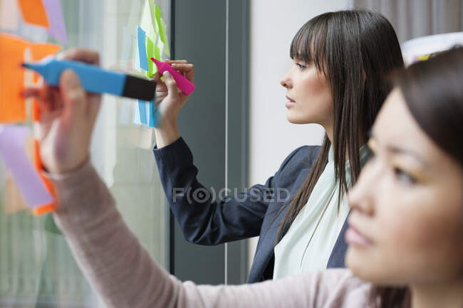 Empresarias escribiendo en notas adhesivas en una oficina - foto de stock
