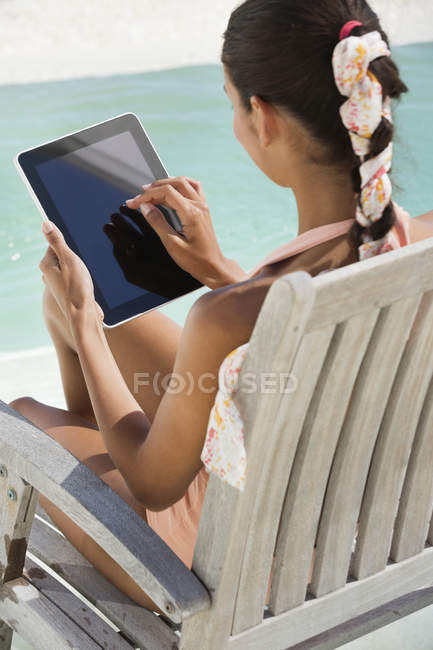 Жінка сидить на кріслі і використовує цифровий планшет на пляжі — стокове фото