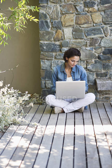 Mujer sentada en el suelo de madera y usando un ordenador portátil en el campo - foto de stock