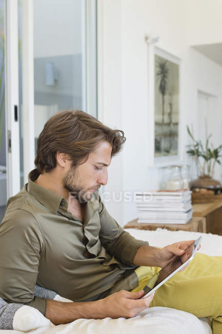 Junger Mann nutzt digitales Tablet zu Hause auf dem Sofa — Stockfoto