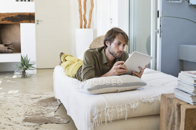 Молодой человек использует цифровой планшет, лежа на кровати — стоковое фото