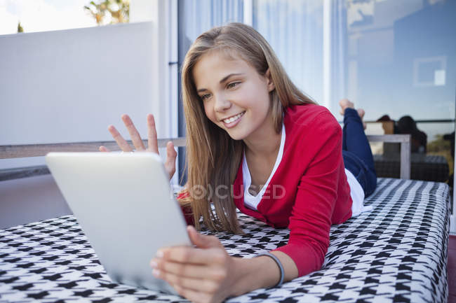 Menina deitada na cama e vídeo conversando no tablet digital — Fotografia de Stock