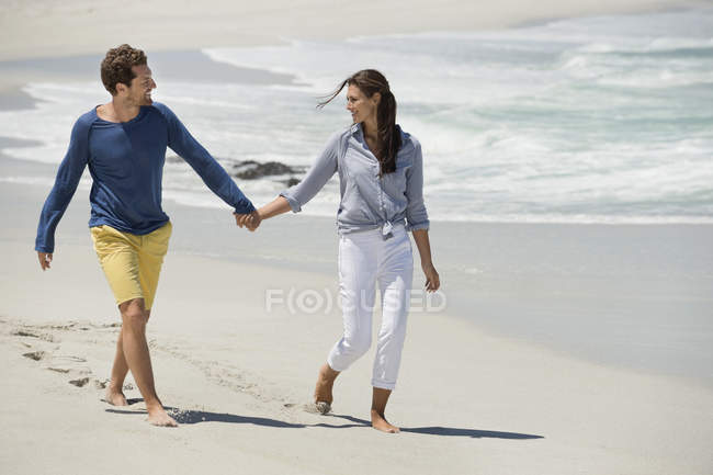 Pareja caminando en playa de arena cogida de la mano - foto de stock