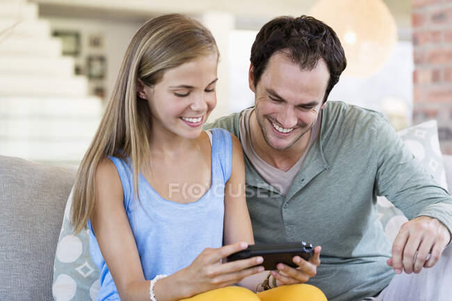 Отец и дочь играют в видеоигру и улыбаются дома — стоковое фото