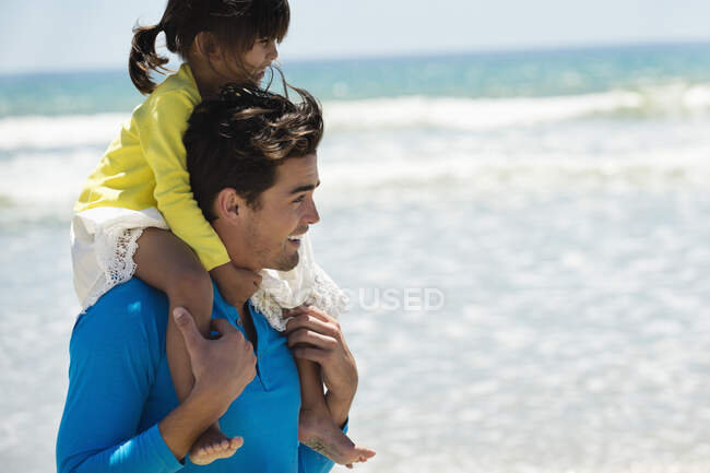 Мужчина несет свою дочь на плечах на пляже — стоковое фото
