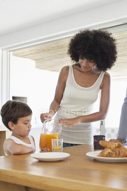 Mulher dando suco de laranja para seu filho — Fotografia de Stock