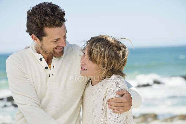 Hombre con su hijo sonriendo en la playa - foto de stock