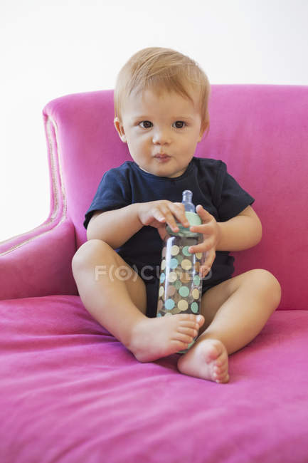 Portrait of cute baby boy sitting with baby bottle in pink armchair — Stock Photo