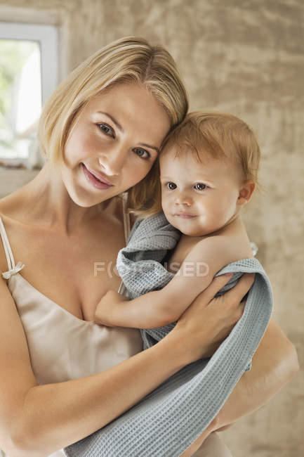 Portrait of young woman holding baby in towel in bathroom — Stock Photo