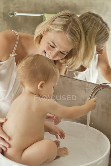 Femme heureuse donnant bain au bébé dans le lavabo — Photo de stock