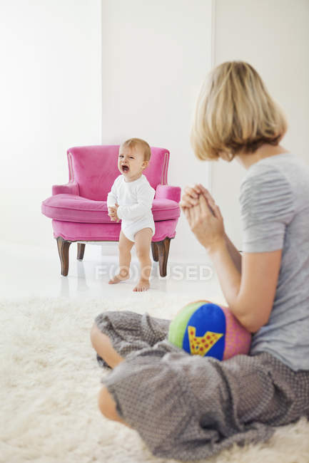 Mujer mirando a bebé llorando mientras está sentado en una alfombra peluda blanca - foto de stock
