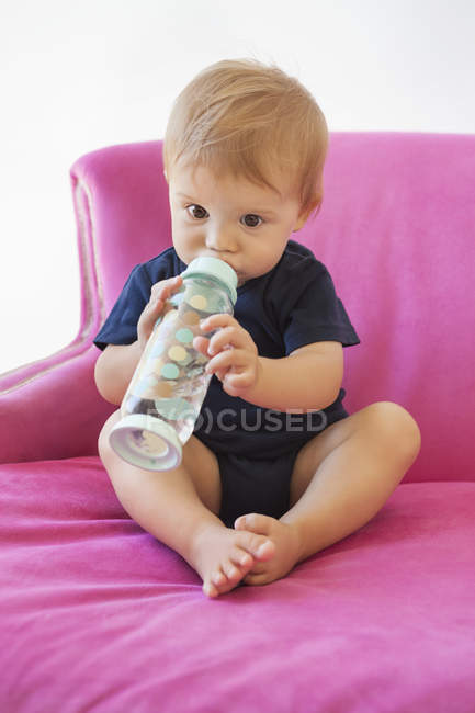 Junge trinkt Wasser aus Flasche im rosa Sessel — Stockfoto