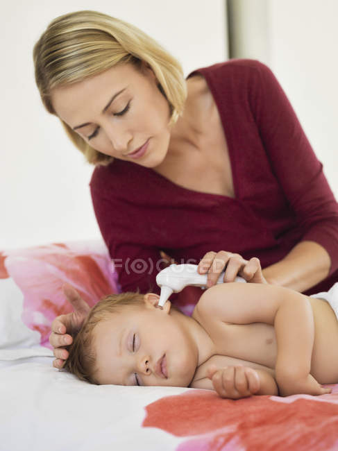 Woman taking baby digital thermometer on bed — Stock Photo