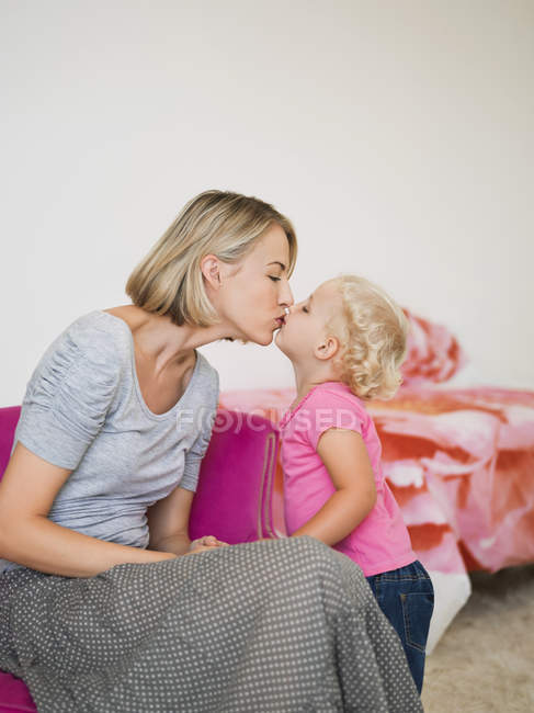 Lindo joven madre e hija besándose en casa - foto de stock
