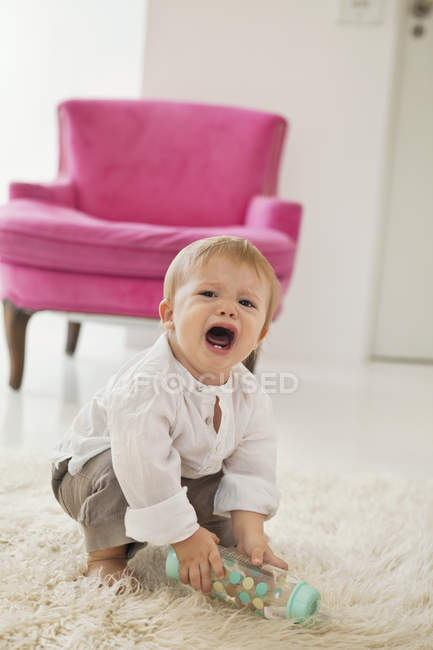 Дитячий хлопчик тримає дитячу пляшку і плаче на білому пухнастому килимі — стокове фото