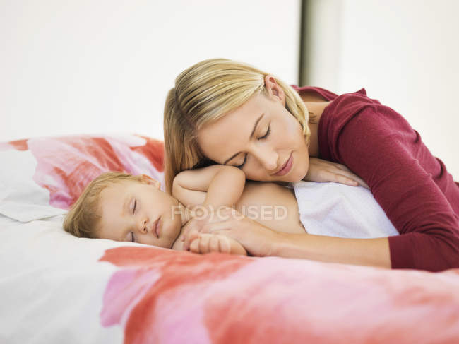 Femme se reposant tête sur l'épaule du bébé dormant sur le lit — Photo de stock