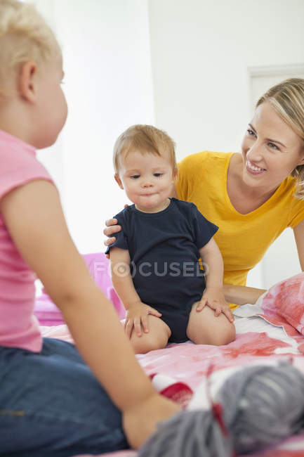 Sonriente mujer jugando con niños en la cama - foto de stock