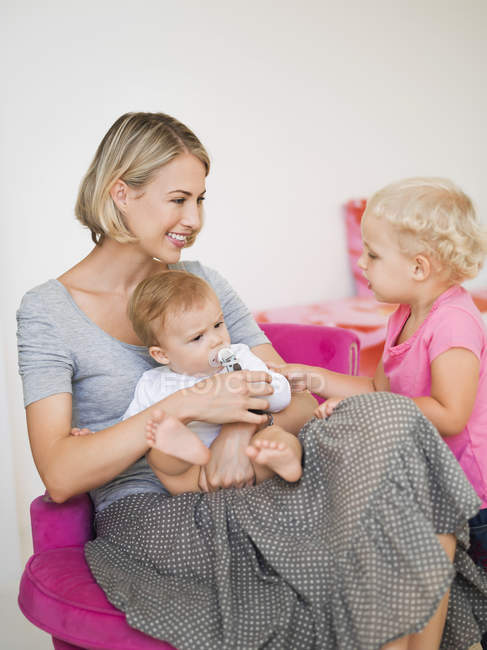 Sorrindo jovem mãe sentada com crianças em casa — Fotografia de Stock