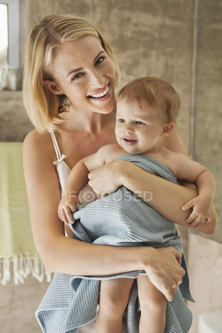 Retrato de mujer joven sosteniendo al bebé en toalla en el baño - foto de stock