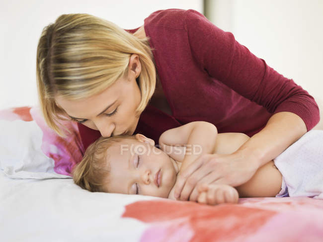 Frau küsst Sohn im Bett schlafend auf die Stirn — Stockfoto