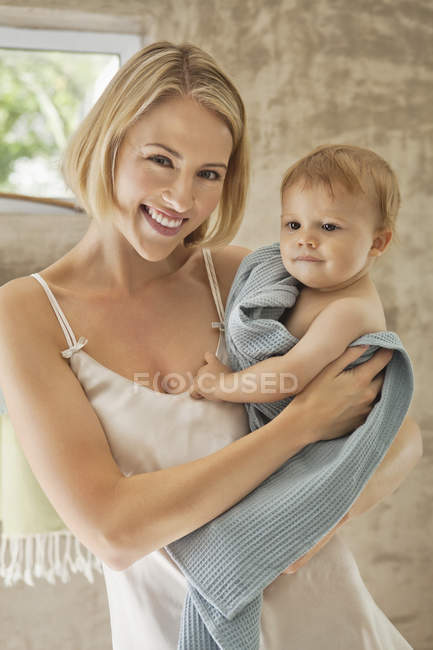 Портрет улыбающейся молодой женщины, держащей ребенка в полотенце — стоковое фото