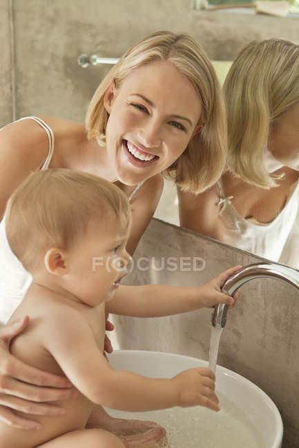 Mulher feliz dando banho ao bebê em lavatório — Fotografia de Stock