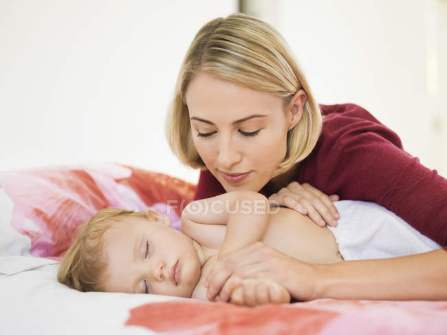 Вдумчивая молодая женщина, глядя на милый ребенок спит на кровати — стоковое фото